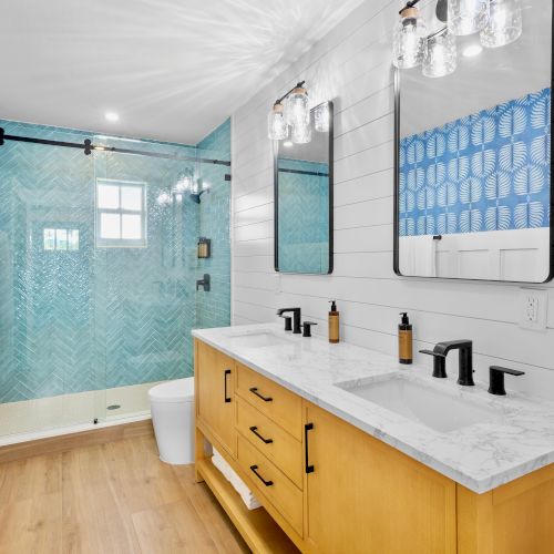 Bright modern bathroom with a blue tiled shower, double mirrors, and a white marble vanity lit by glass fixtures.