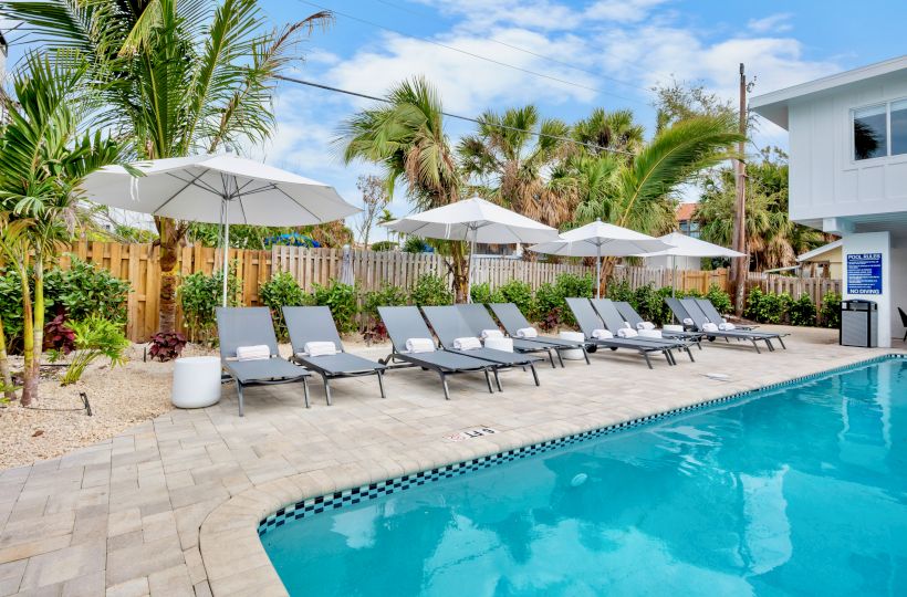 A sunny backyard pool area with blue water, white lounge chairs under umbrellas, lush palm trees, and fencing for a tropical retreat.