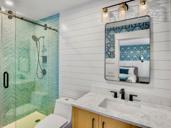 Modern bathroom with a glass shower, green tile walls, and a marble vanity with a large mirrored wall and pendant lights.