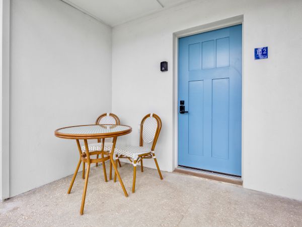 A small patio nook with a round wooden table and chairs beside a blue paneled door and wall art.