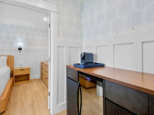 A bright room with a bed, dresser, and a coffee machine on a wooden counter against patterned wallpaper.