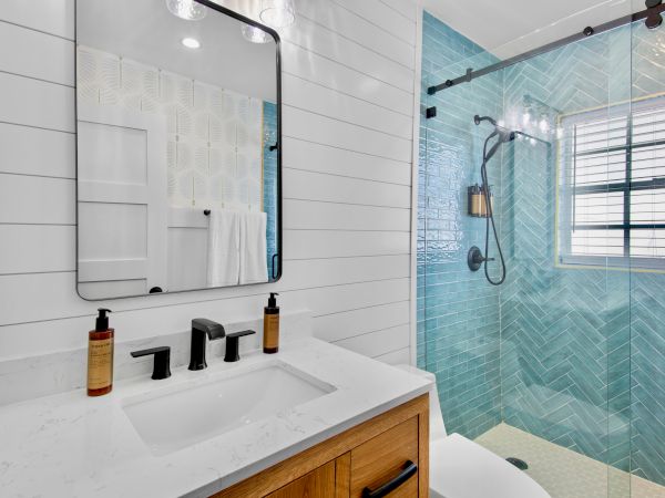 A modern bathroom with a white sink and toiletries, a glass mirror, and a tiled shower with a rainfall showerhead.