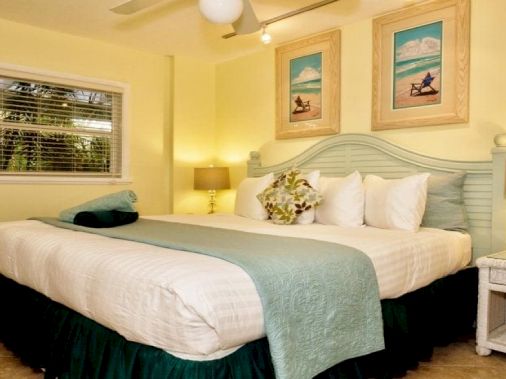 A bright coastal-style bedroom with a neatly made bed, white headboard, teal bedding, and nautical wall art, lit by lamps.
