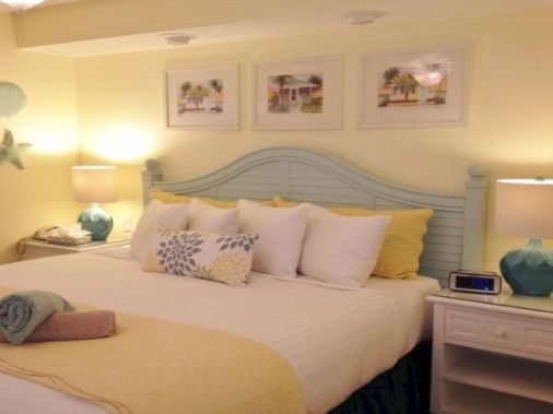 A cozy bedroom with a neatly made bed, nightstands, lamps, framed wall art, and decorative starfish and seashell accents.