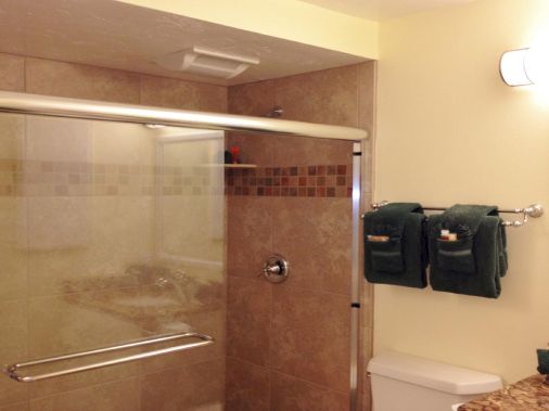 A tiled bathroom with a glass shower, grab bars, folded towels on a rack, and a toilet partially visible.