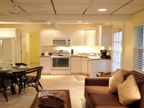 Bright open-plan kitchen with white cabinets, oven, and coffee makers, plus a dining table and brown couch in a living area.