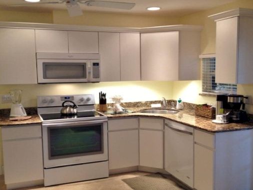 A bright, modern kitchen with white cabinets, a granite countertop, stove, microwave, and appliances.