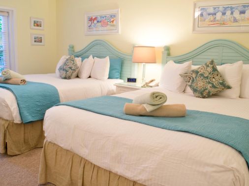 A bright guest bedroom with two made twin beds, teal-and-white linens, pillows, and bedside lamps.