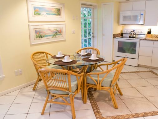 A bright kitchen with a small dining table set with cups and chairs, plus a stove, oven, and microwave on the counter.