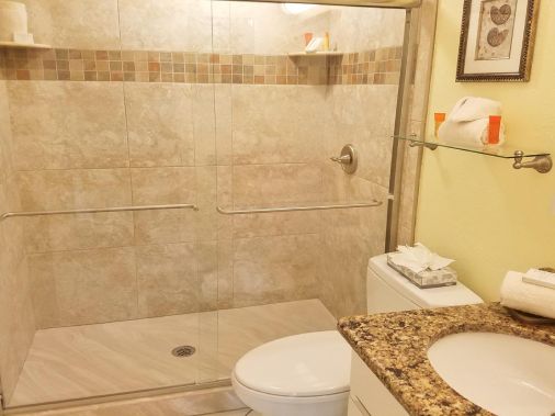 A tidy bathroom with a glass shower, toilet, granite sink, and neatly folded towels.