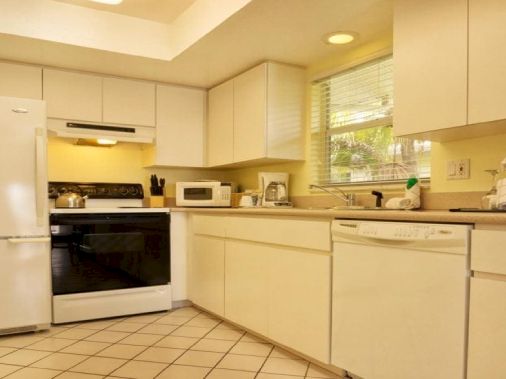 A bright, modern kitchen with white cabinets, a stove, oven, microwave, and a tiled floor.