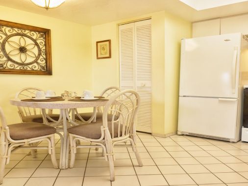 A sunny dining-kitchen area with a round table and wicker chairs, plus a white refrigerator and stove.