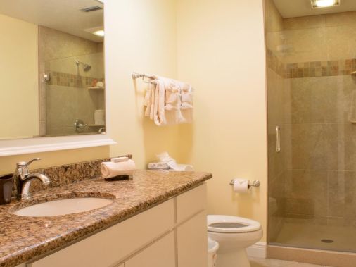 A modern bathroom with a double sink vanity, folded towels, a toilet, and a glass-walled shower.