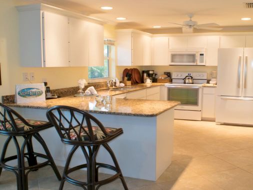 Bright kitchen with a granite island, two bar stools, white cabinets, and appliances in a clean, sunny space.