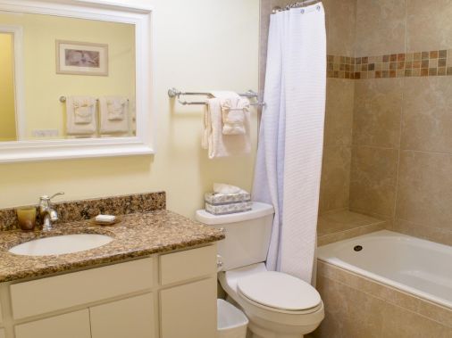 A clean bathroom with a granite vanity, toilet, bathtub, and white towels on the wall.