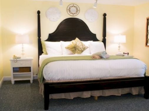 A bright bedroom with a dark wooden bed, white bedding, two nightstands, lamps, and framed wall art, all in a cozy setting.