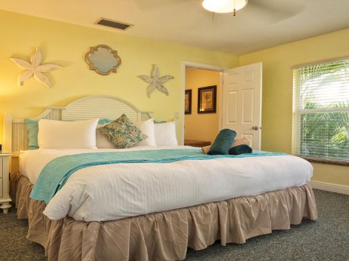 A bright, beach-themed bedroom with a double bed, teal accents, and a large window showing palm views.