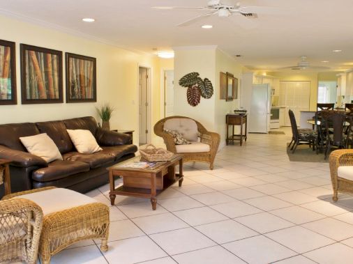 A bright living room with leather sofa, wicker chairs, a coffee table, and a dining area in the background.