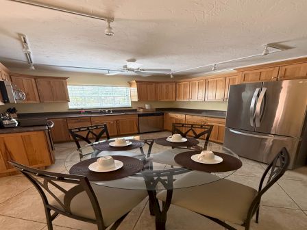 Wood-paneled kitchen with appliances and an oval dining table for six chairs, lit by ceiling lights and a window.