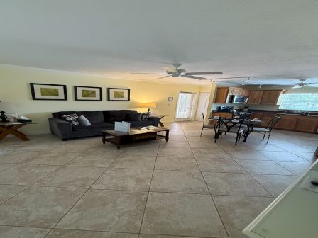 A bright open-plan living room with gray sofa and coffee table, connected to a wooden kitchen with bar stools and appliances.