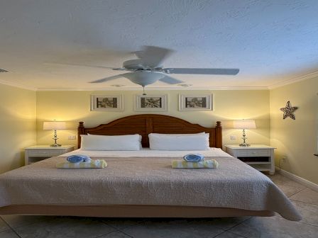 A neatly made bedroom with a large wooden headboard, two nightstands, a ceiling fan, and framed wall art.