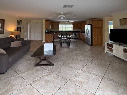 Spacious living room and kitchen with tiled floors, ceiling fans, gray sofa, and wooden cabinets.
