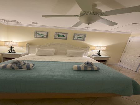 A tidy hotel-style bedroom with a large bed, ceiling fan, twin nightstands, wall art, and neatly folded towels on the covers.