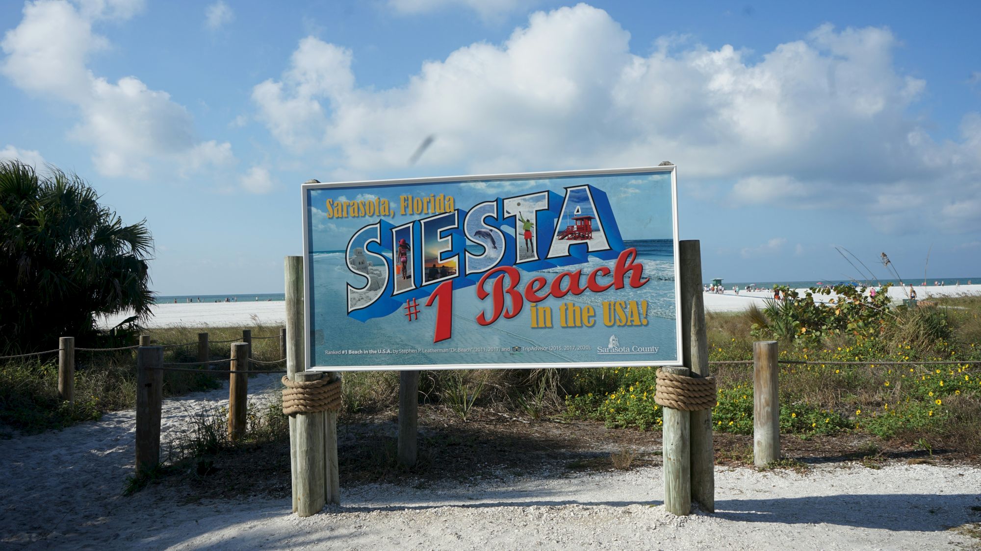 A seaside sign reads &ldquo;Sarasota, Florida #1 Beach Retreat in the USA&rdquo; with a beach scene under a bright blue sky.