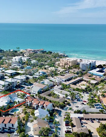 Aerial view of a seaside resort with the ocean horizon and rooftops below, with a highlighted property outlined in red.