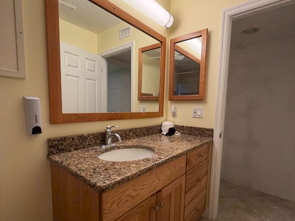 A bathroom vanity with a granite countertop, mirrors, ceiling light, sink, faucet, and tiled floor.